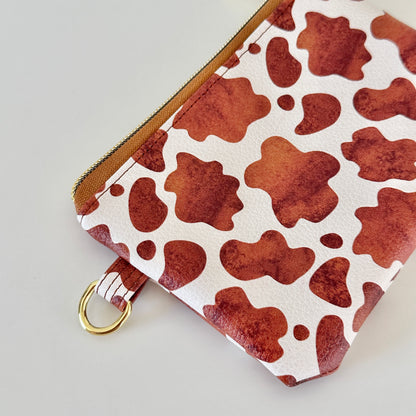 Cow print coin purse with coins and cards on a white background