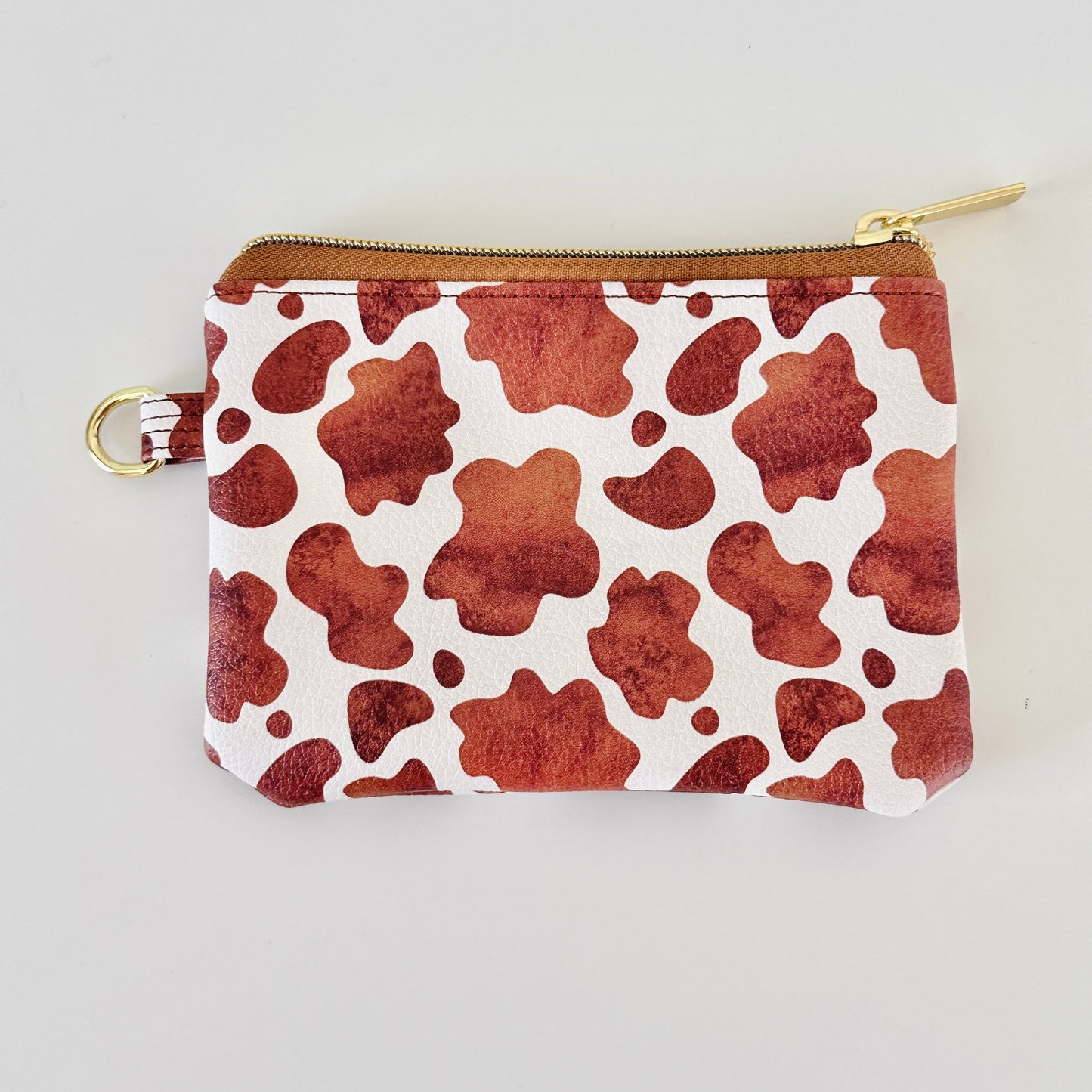 Cow print coin purse with coins and cards on a white background