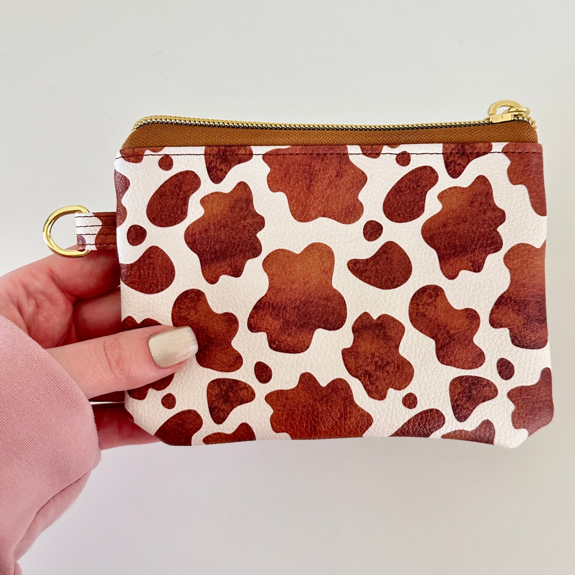 Cow print coin purse with coins and cards on a white background