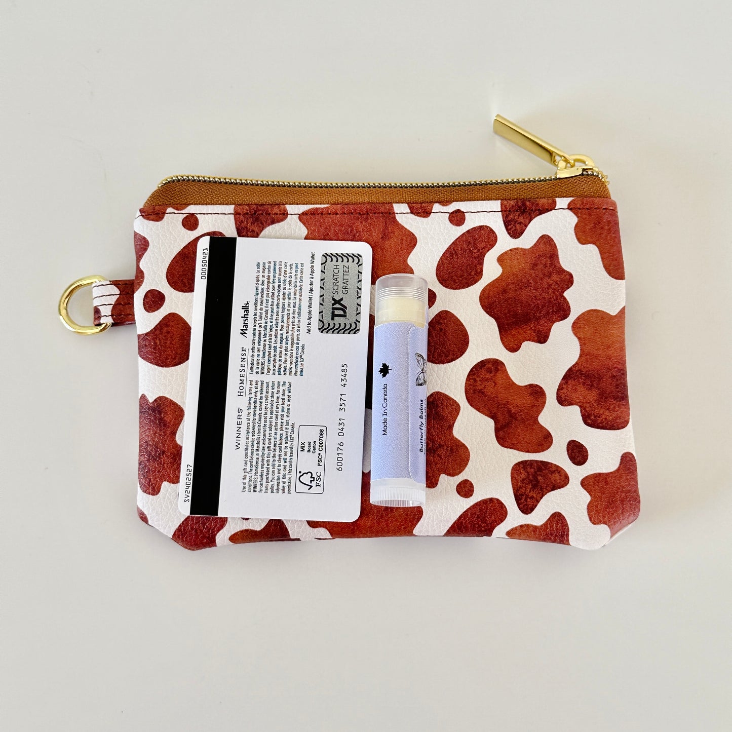 Cow print coin purse with coins and cards on a white background