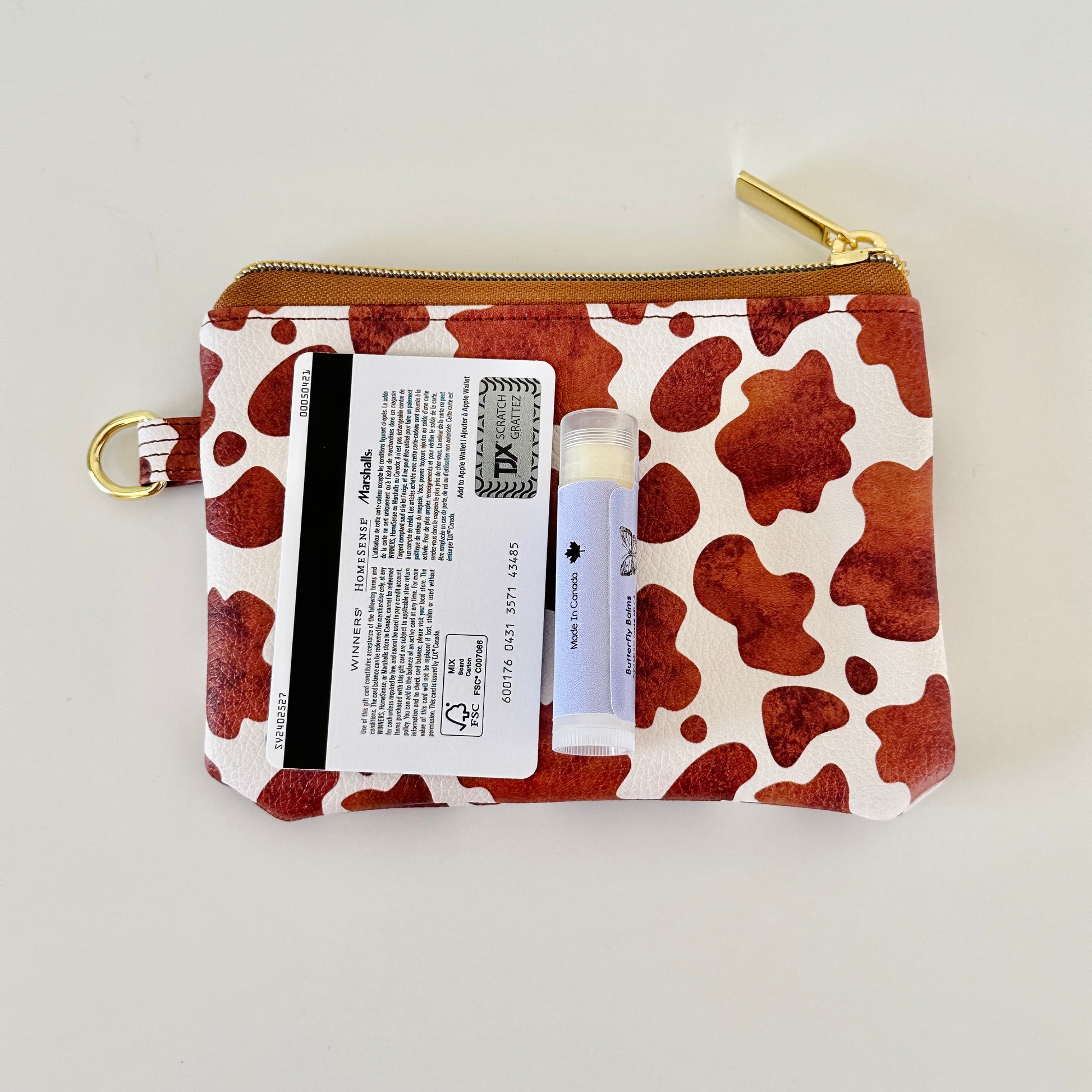 Cow print coin purse with coins and cards on a white background