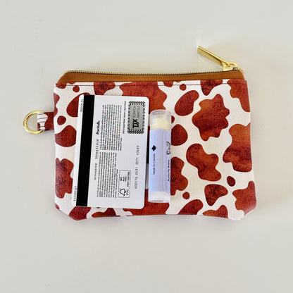 Cow print coin purse with coins and cards on a white background