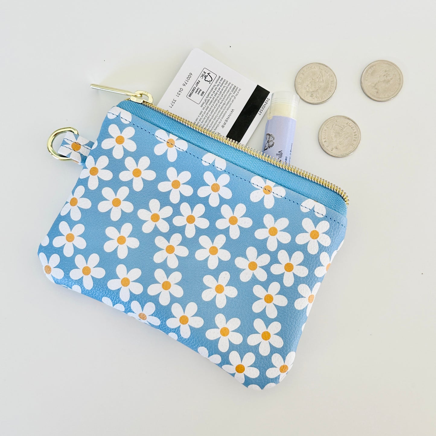 Blue floral daisy patterned coin purse with coins and cards on a white background