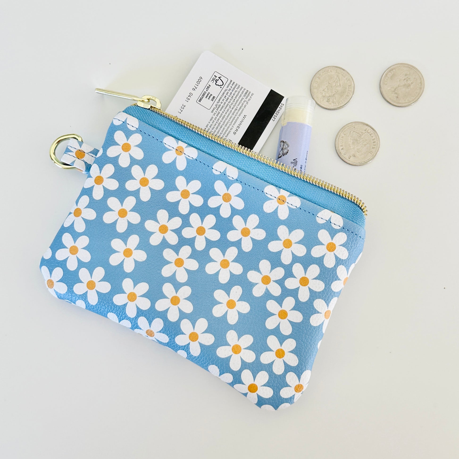Blue floral daisy patterned coin purse with coins and cards on a white background