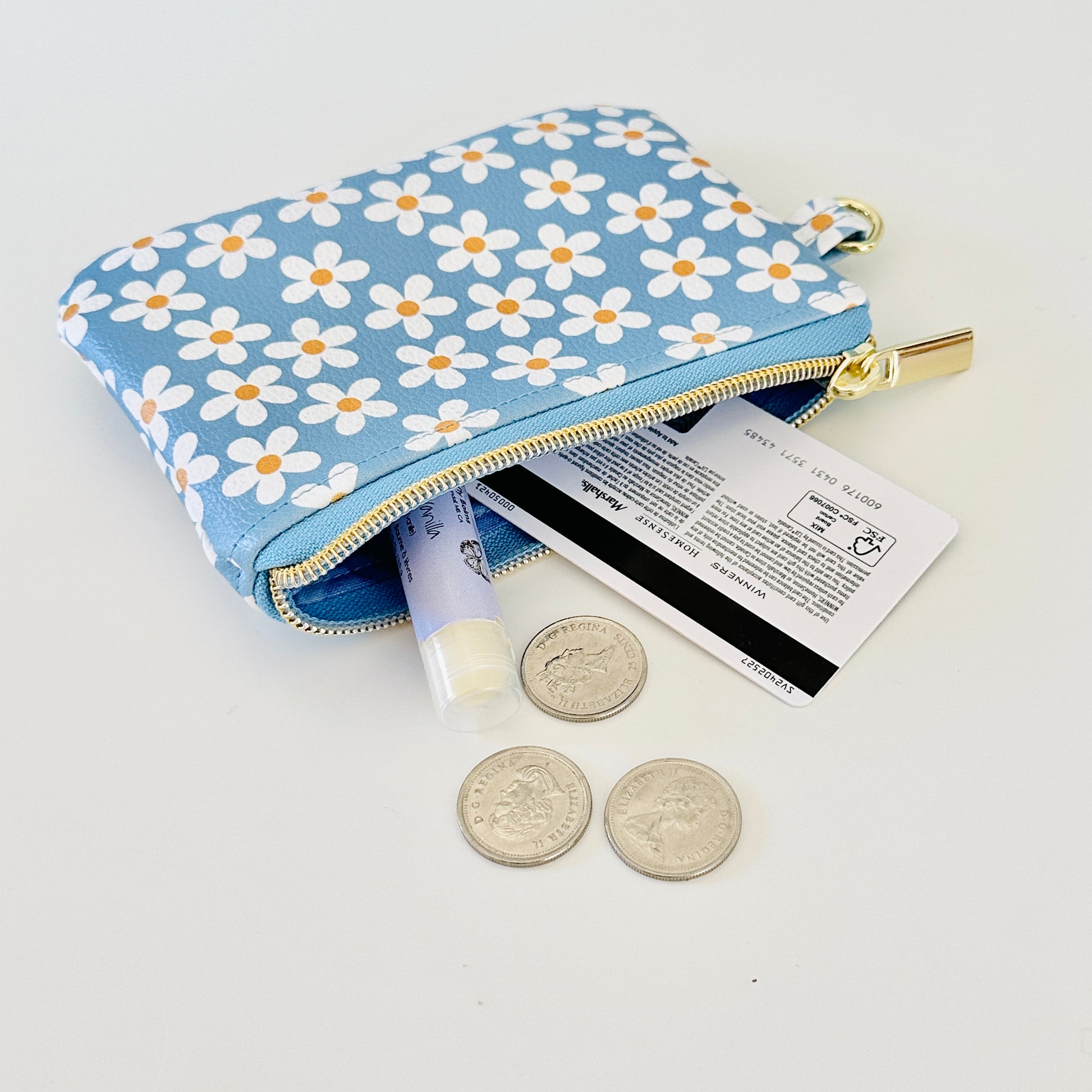 Blue floral daisy patterned coin purse with coins and cards on a white background