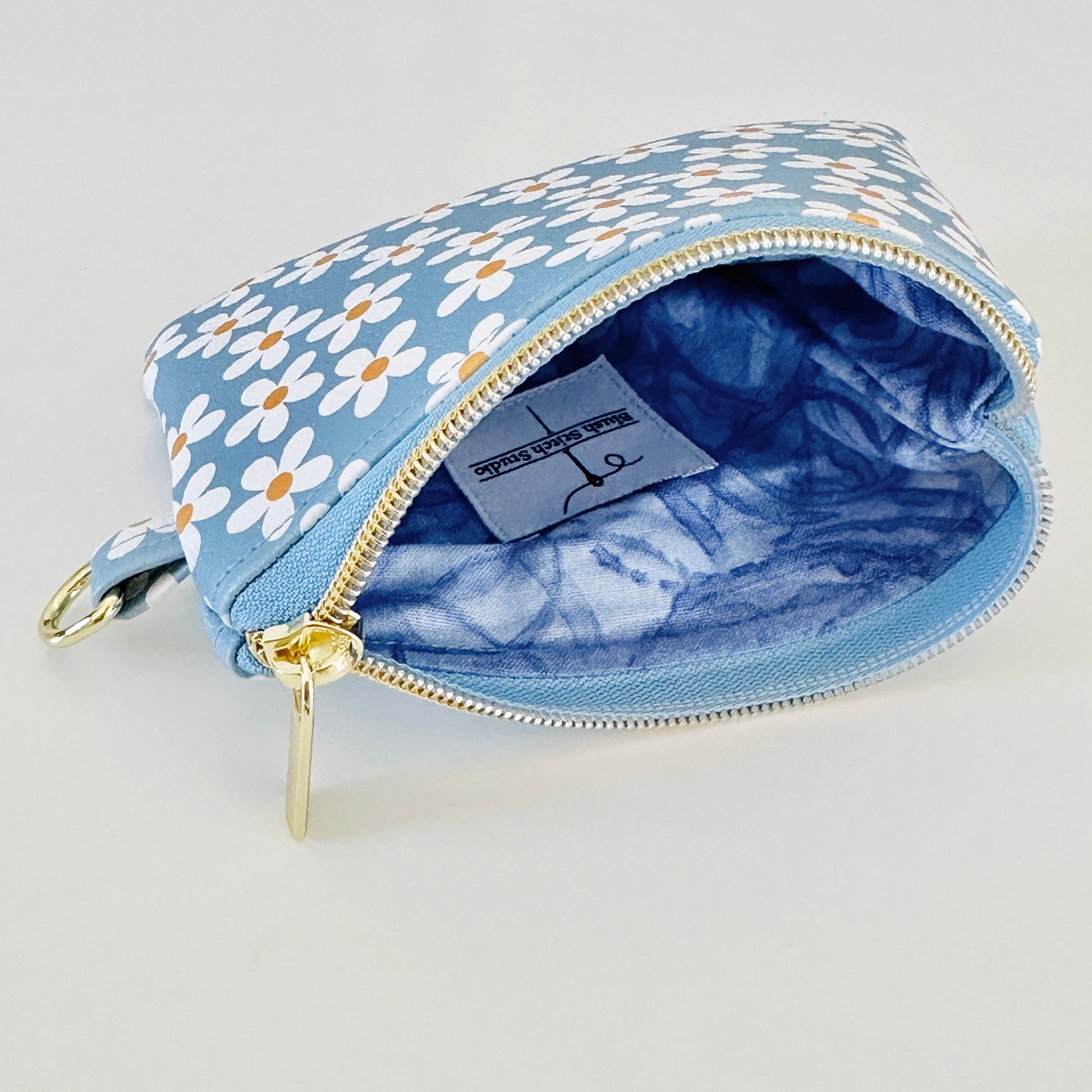 Blue floral daisy patterned coin purse with coins and cards on a white background