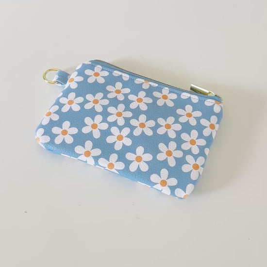 Blue floral daisy patterned coin purse with coins and cards on a white background