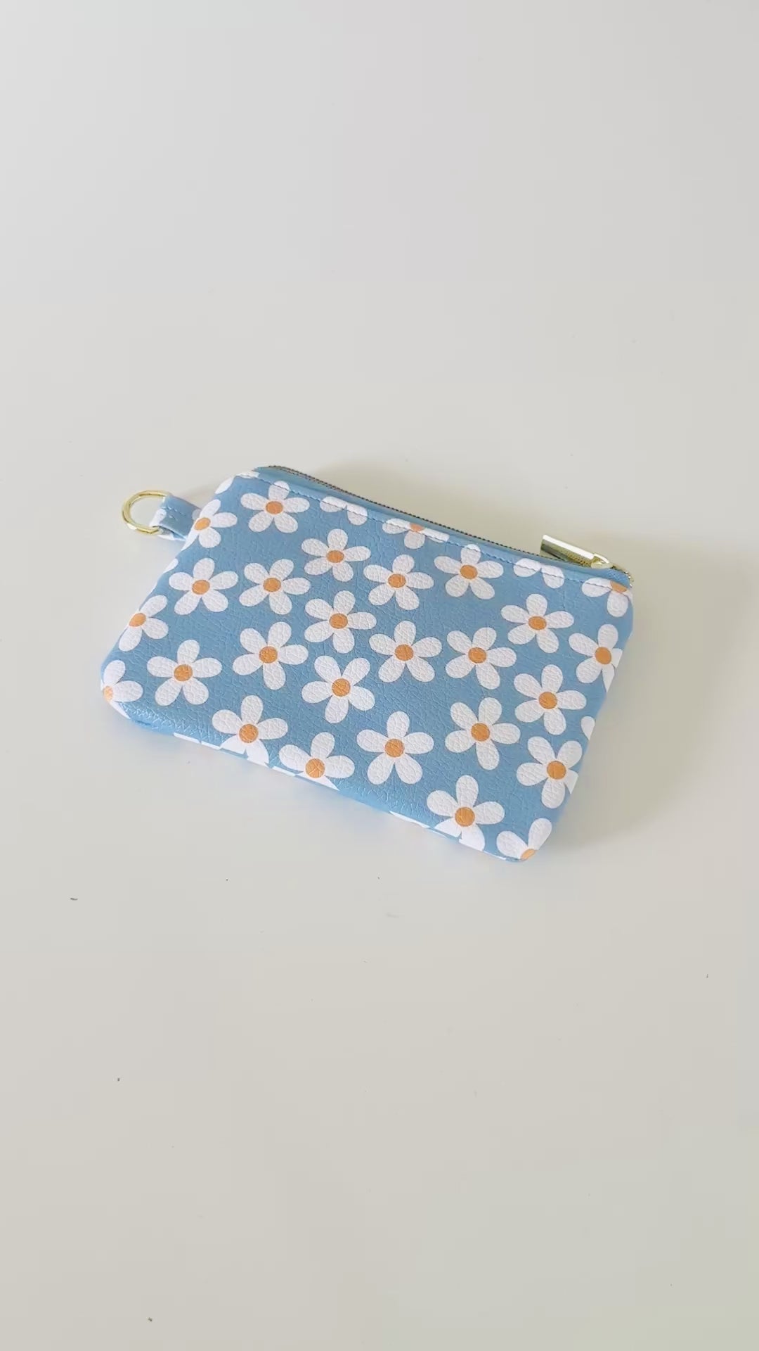 Blue floral daisy patterned coin purse with coins and cards on a white background