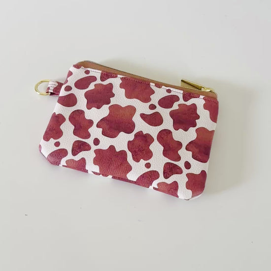 Cow print coin purse with coins and cards on a white background