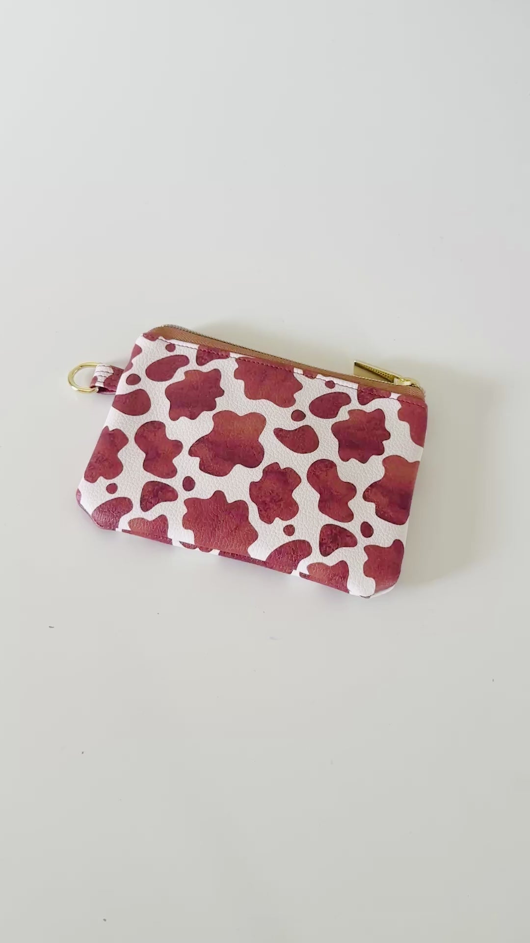 Cow print coin purse with coins and cards on a white background