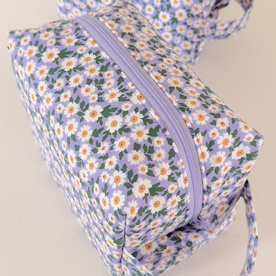 Set of floral-patterned pouches with a hand holding one of them on a light background