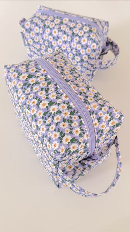 Set of floral-patterned pouches with a hand holding one of them on a light background