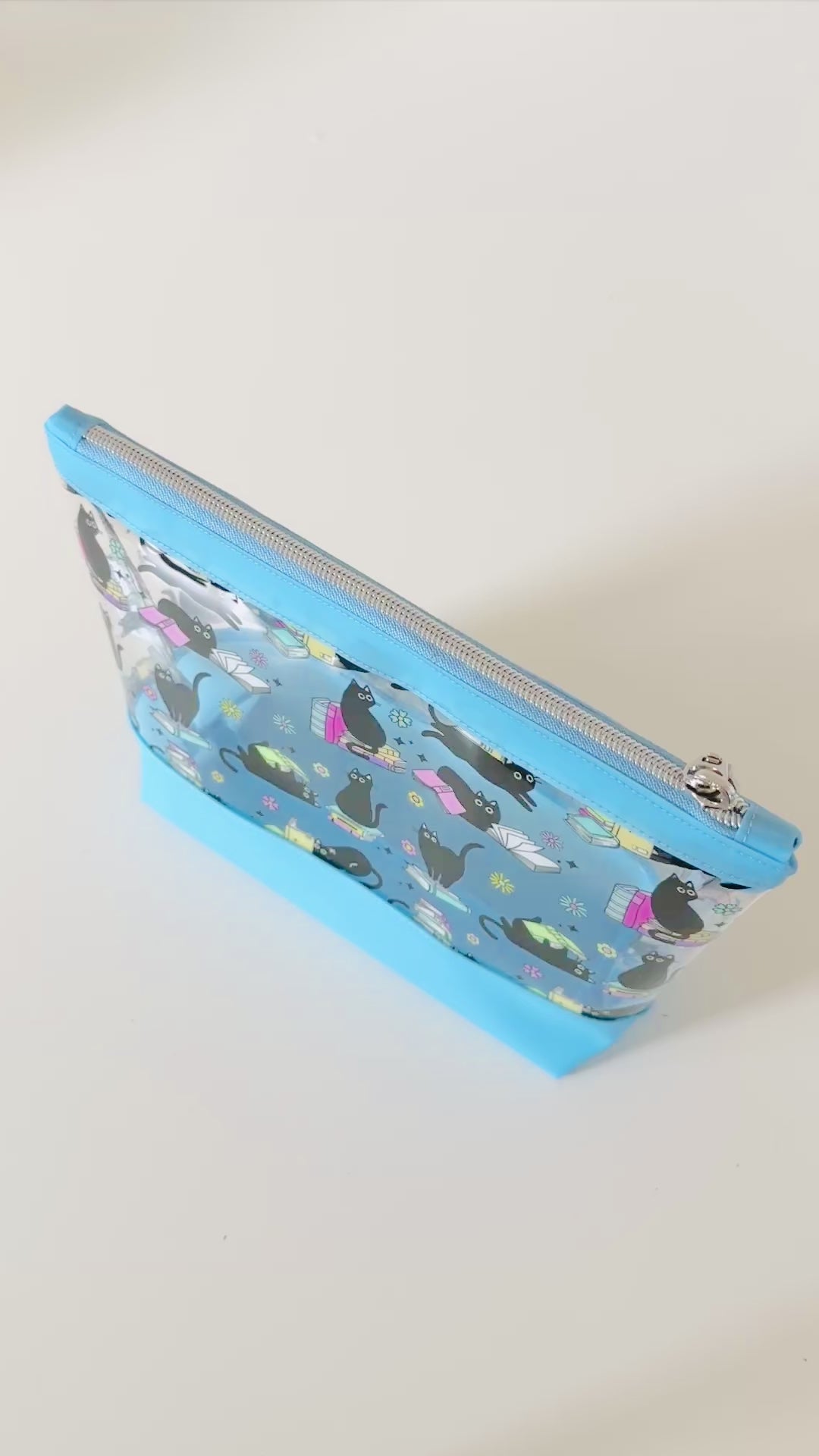 clear makeup bag with a black cat and book pattern pink bottom