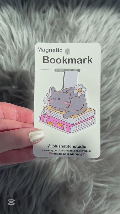 Magnetic bookmark with a cat design on a white card held by a hand against a fluffy gray background.