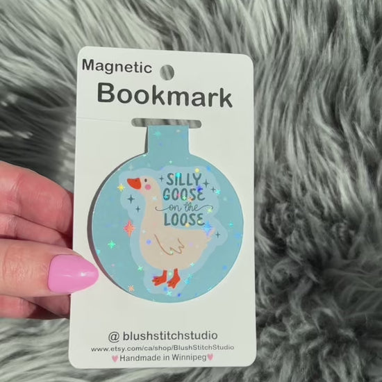 Magnetic bookmark with a silly goose design on a card held by a hand against a fluffy gray background