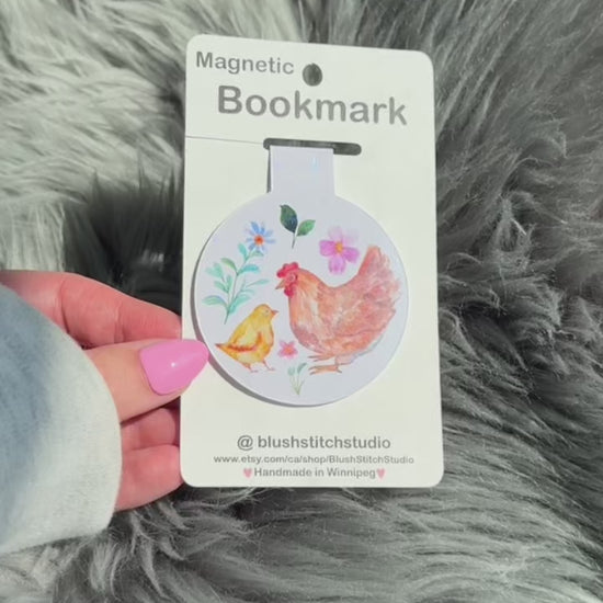 Magnetic bookmark with chicken design on a card held by a hand against a fluffy gray background