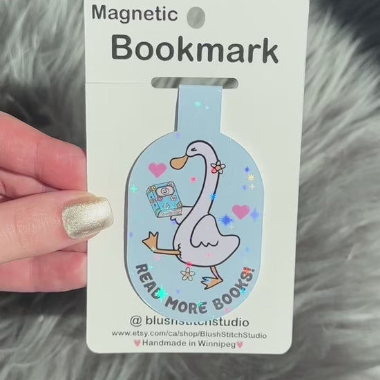 Magnetic silly goose bookmark with a cartoon goose holding a book on a card, held against a textured gray background.