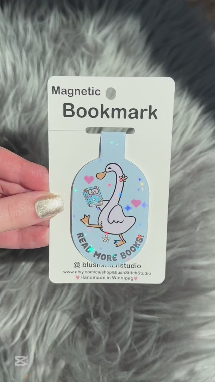 Magnetic silly goose bookmark with a cartoon goose holding a book on a card, held against a textured gray background.