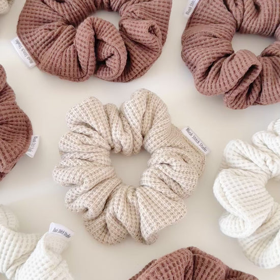 Three neutral waffle textured scrunchies in beige, brown, and light brown on a white background.