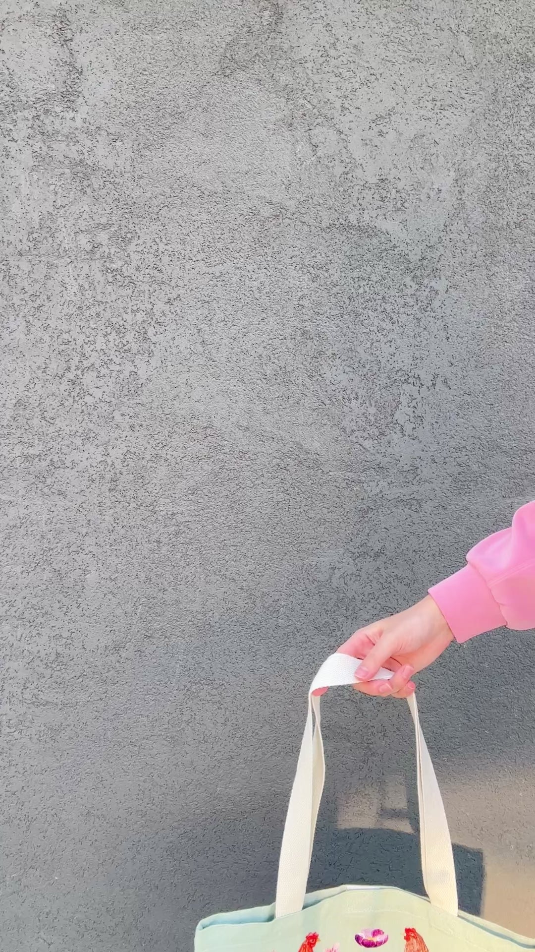 Tote bag with chicken and wildflower design held by a person in a pink jacket.