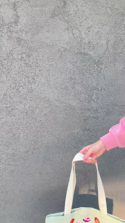 Tote bag with chicken and wildflower design held by a person in a pink jacket.