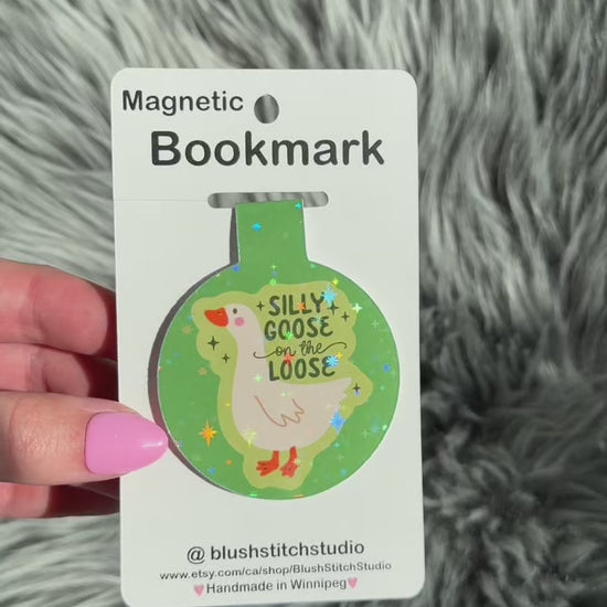 Magnetic bookmark with 'Silly Goose on the Loose' design held by a hand against a textured gray background