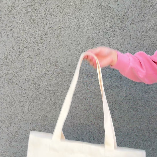 Tote bag with black cat and book illustrations held by a person wearing a pink jacket.